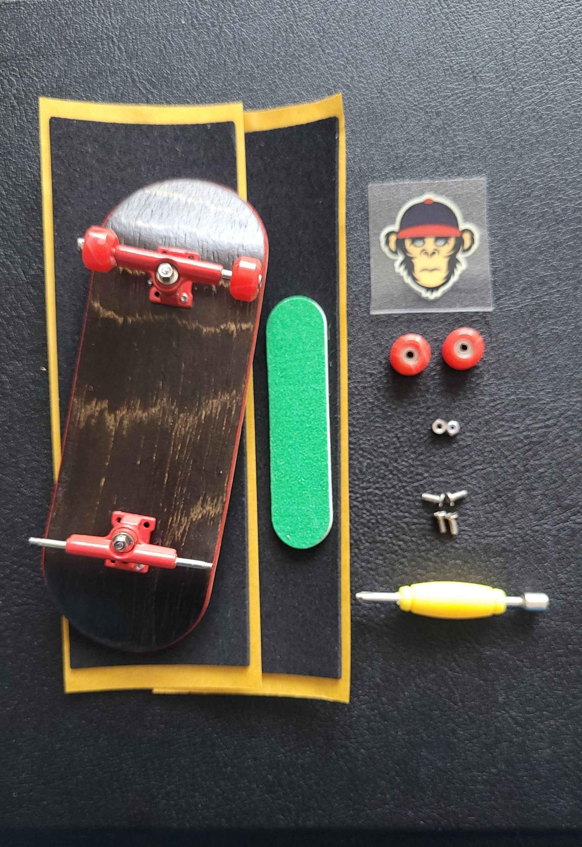 Custom fingerboard kit with wooden deck, red trucks, wheels, grip tape, and a monkey sticker.