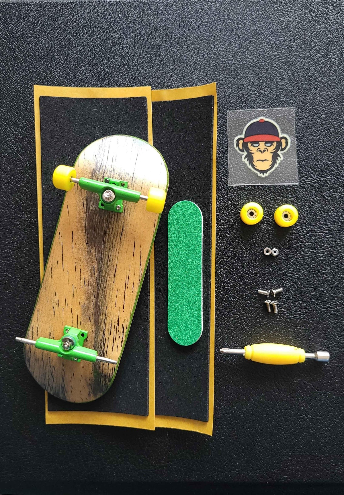 Custom fingerboard kit with a wooden deck, green trucks, yellow wheels, and grip tape.