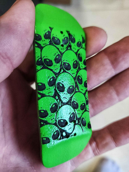 Custom green fingerboard deck featuring a pattern of black alien faces