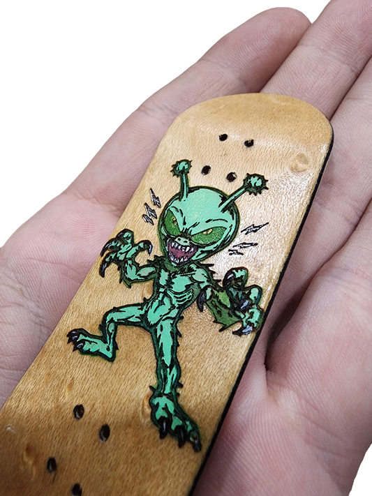 Handmade custom fingerboard deck with a green alien graphic held in hand.