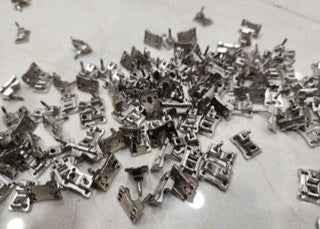 A collection of small, silver metal fingerboard truck parts scattered on a white surface.