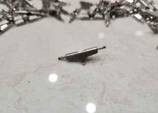 Close-up of a metal fingerboard truck part on a white marble surface.