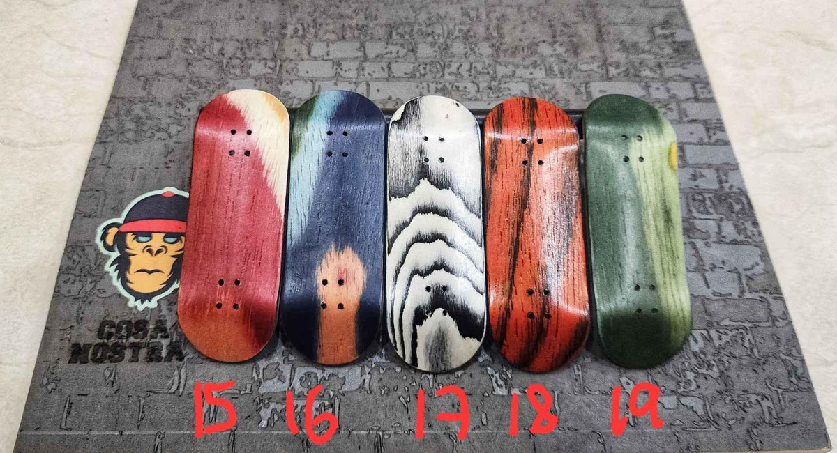 Five handmade custom fingerboard decks with various wood grain patterns on a textured background.
