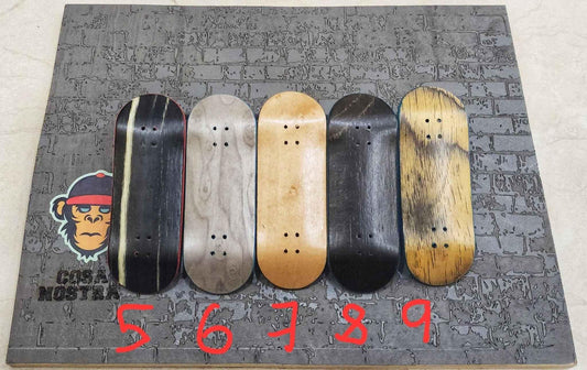 Five handmade custom fingerboard decks in various wood grains on a textured grey background.