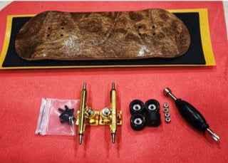 Handmade wooden fingerboard deck with gold trucks, black wheels, and a tool on a red background