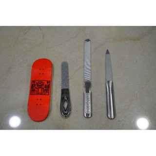 A red fingerboard deck alongside a metal file and two shaping tools on a light surface.
