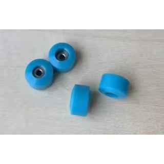 Four small blue fingerboard wheels on a light wooden surface.