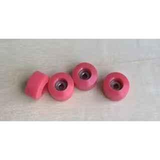 Four pink miniature fingerboard wheels on a light wooden surface.