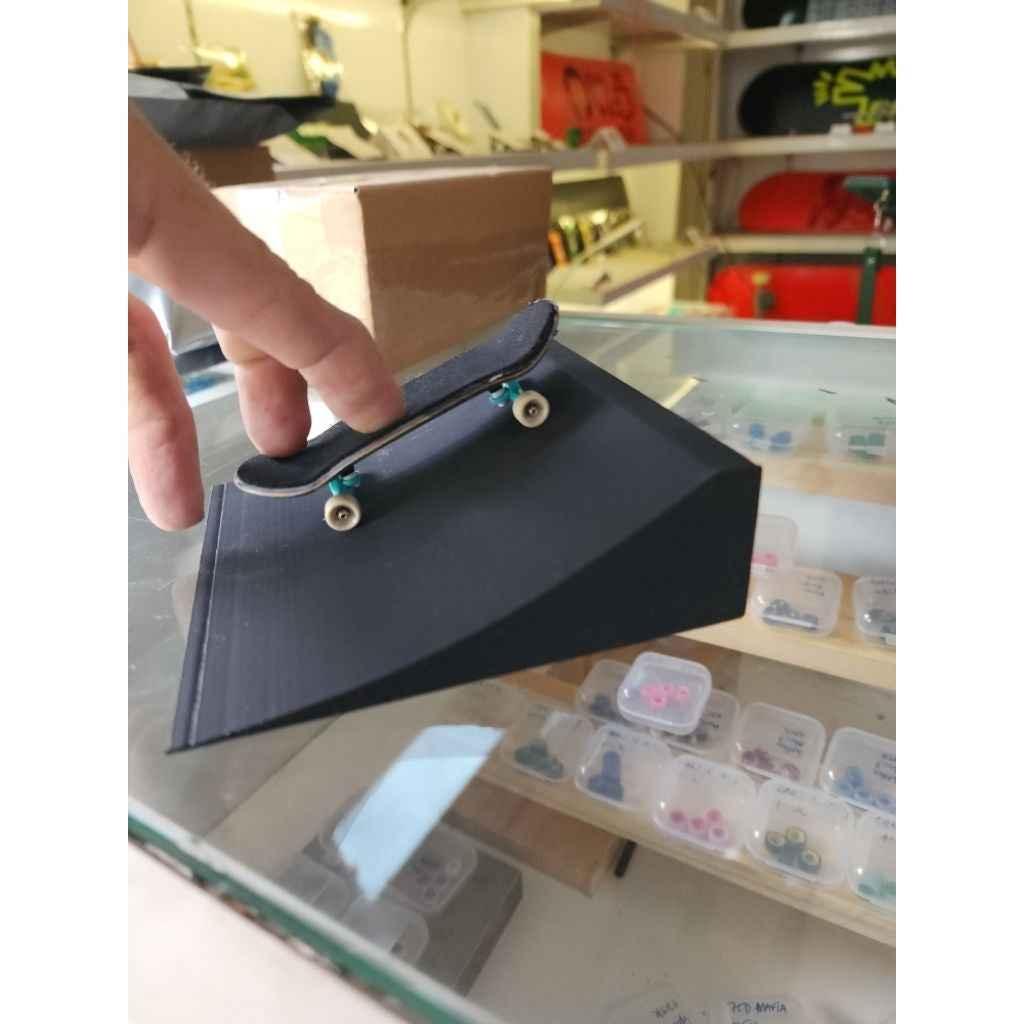 Hand performing a trick with a custom fingerboard on a black miniature skate ramp.