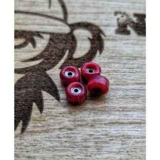 Four small red fingerboard bearings on a light wood surface.
