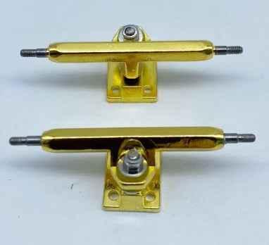 Two gold-colored fingerboard trucks with silver hardware on a white background