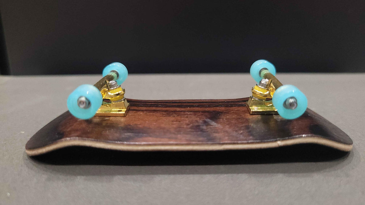 A handmade custom fingerboard deck with gold trucks and light blue wheels.