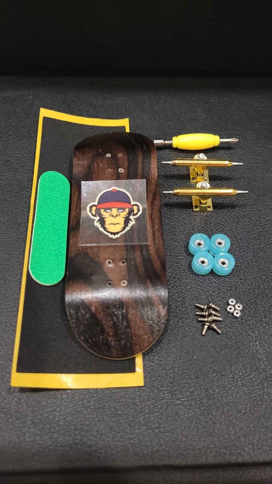 Fingerboard kit with wood deck, yellow trucks, blue wheels, and green grip tape.
