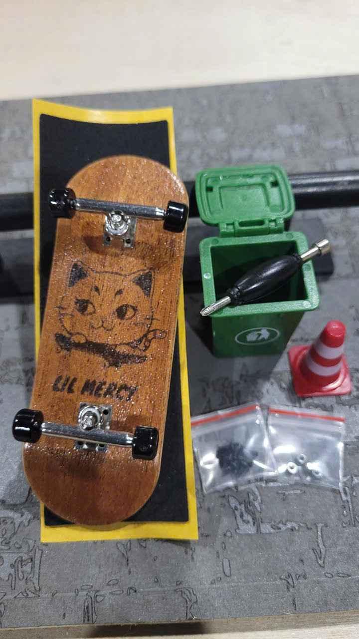 Custom wooden fingerboard deck with cat graphic, mini green trash can, and accessories.