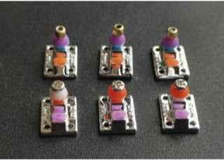 Six colorful custom fingerboard trucks with purple and orange bushings on a dark background