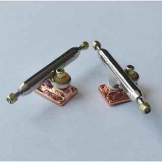 Two custom metal fingerboard trucks with copper bases on a white background