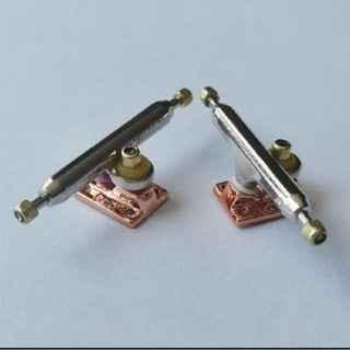 Pair of custom metal fingerboard trucks with polished axles and copper baseplates