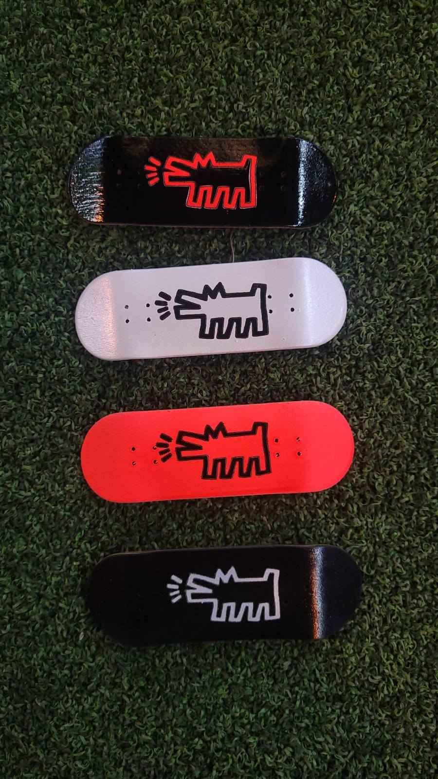 Four custom fingerboard decks in black, white, and red with a graphic design on green grass.