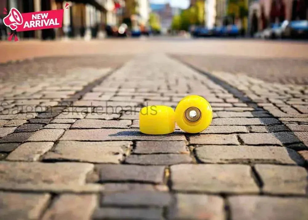 Two bright yellow fingerboard wheels on a cobblestone street.