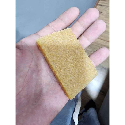 A rectangular piece of yellow sponge held in a person's hand.