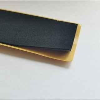 Close-up of a black grip tape sheet on a yellow backing for a fingerboard deck.