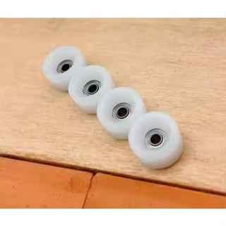 Four white miniature fingerboard wheels arranged in a diagonal line on a wooden surface.