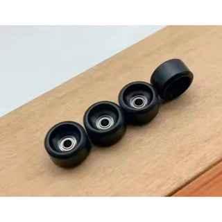 Four black miniature fingerboard wheels arranged in a row on a wooden surface.