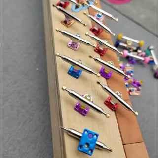 Assorted colorful custom fingerboard trucks and hardware on a wooden display stand.