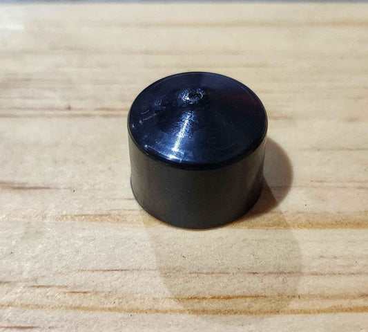 Close-up of a small, cylindrical black plastic accessory on a light wood surface.