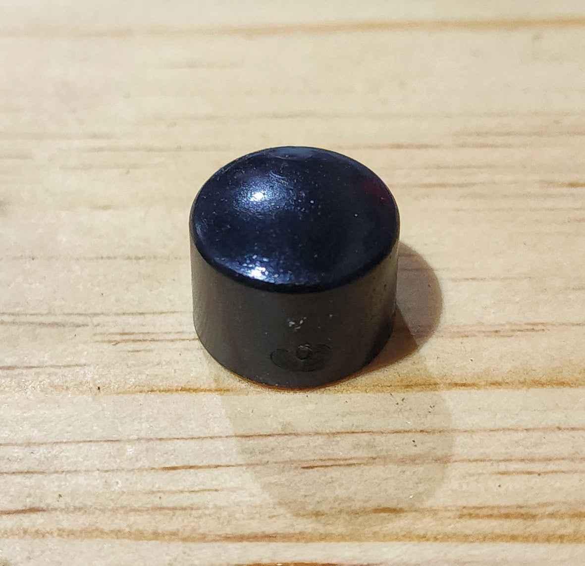 Small black dome-shaped fingerboard accessory on a light wood surface