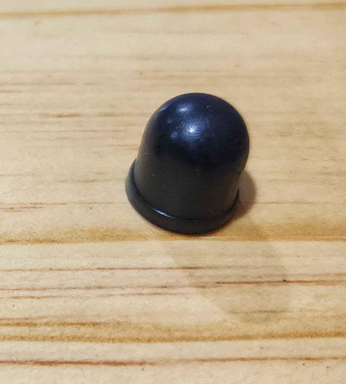 Black rubber fingerboard grip cap on a light wooden surface