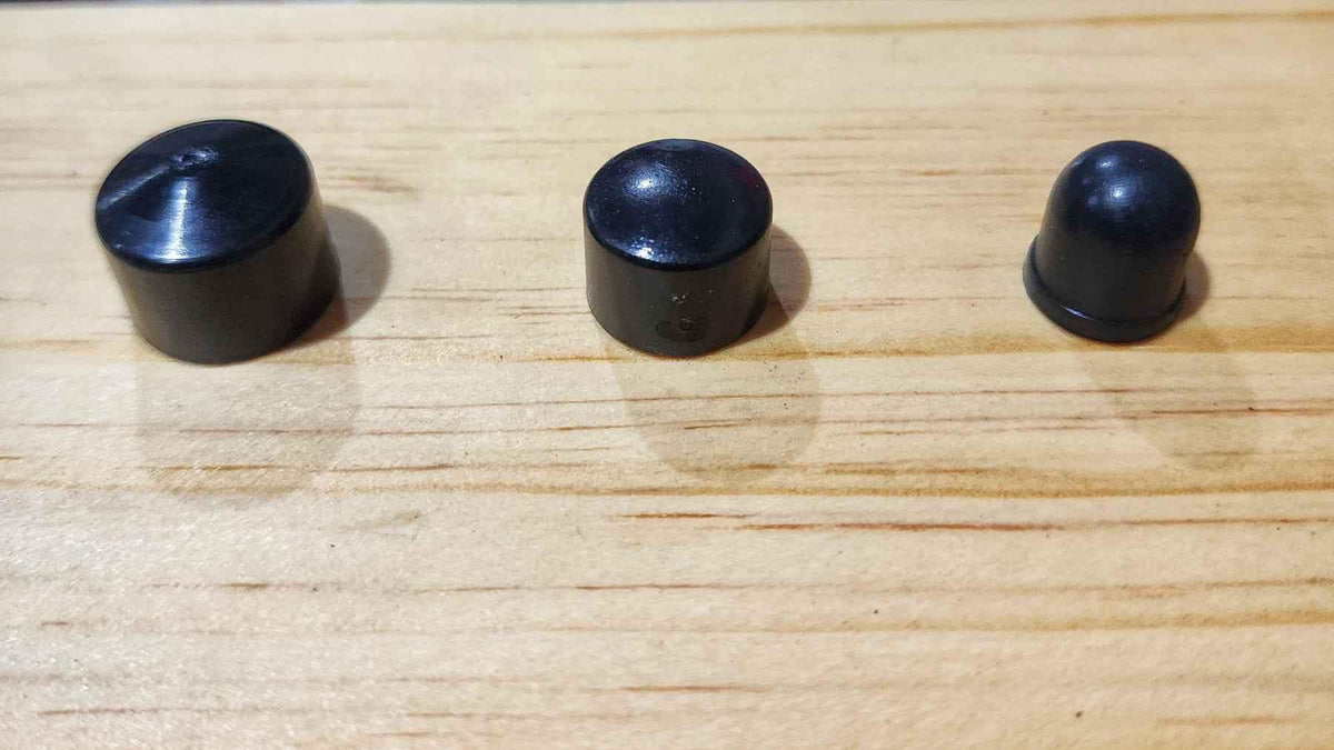 Three black plastic fingerboard grip caps of different sizes on a wooden surface