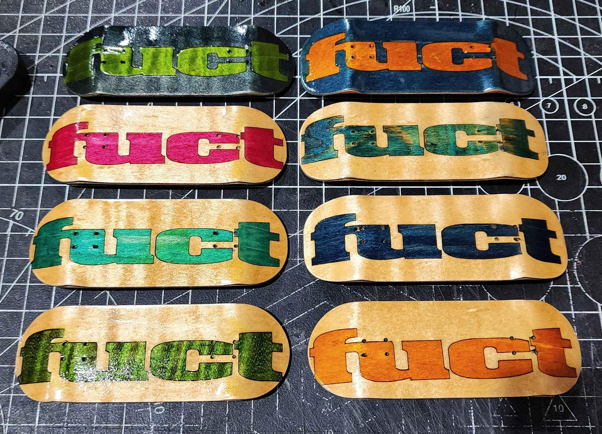 Eight custom handmade fingerboard decks with colorful graphic prints on a cutting mat.