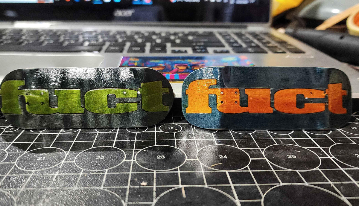 Two custom fingerboard decks with 'fuct' graphics on a cutting mat.