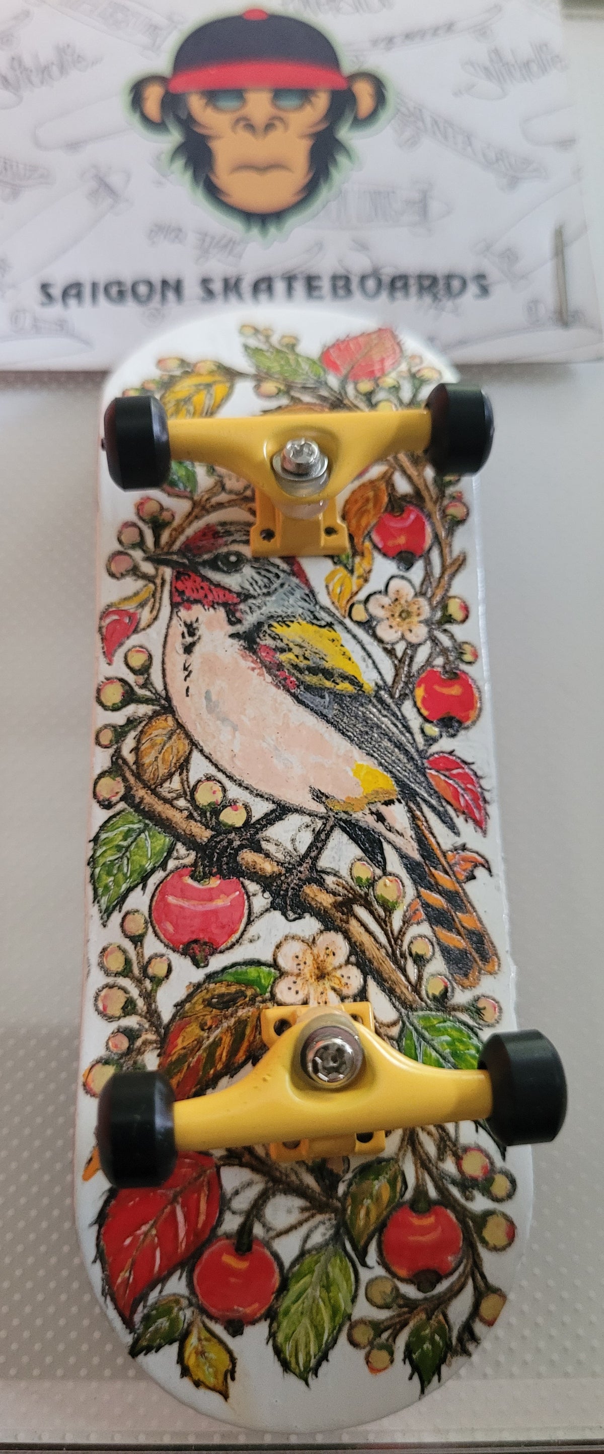 Top view of complete finger skateboard, bird floral and cherry graphic deck