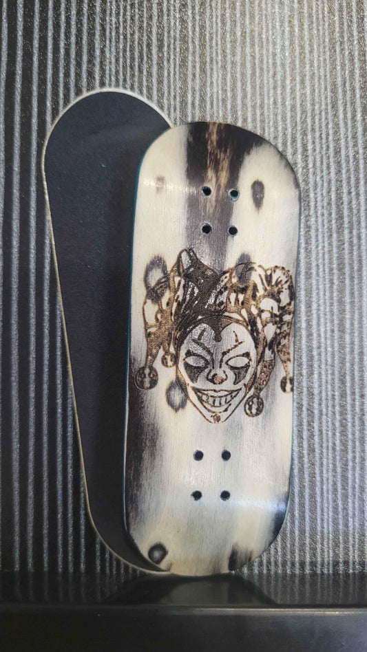Custom handmade fingerboard deck with a dark jester graphic design on white wood.