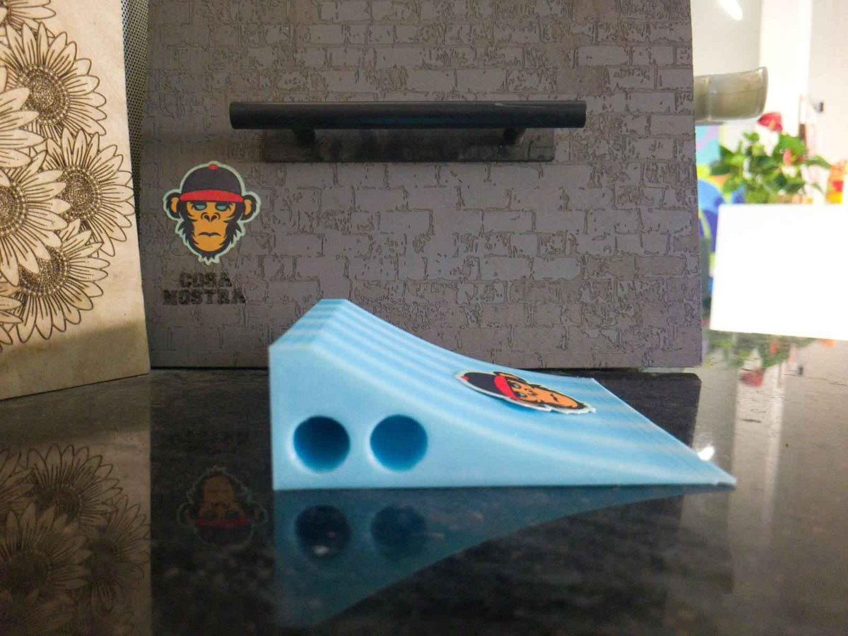 Light blue fingerboard mini ramp wedge with a graphic sticker on a dark reflective surface.