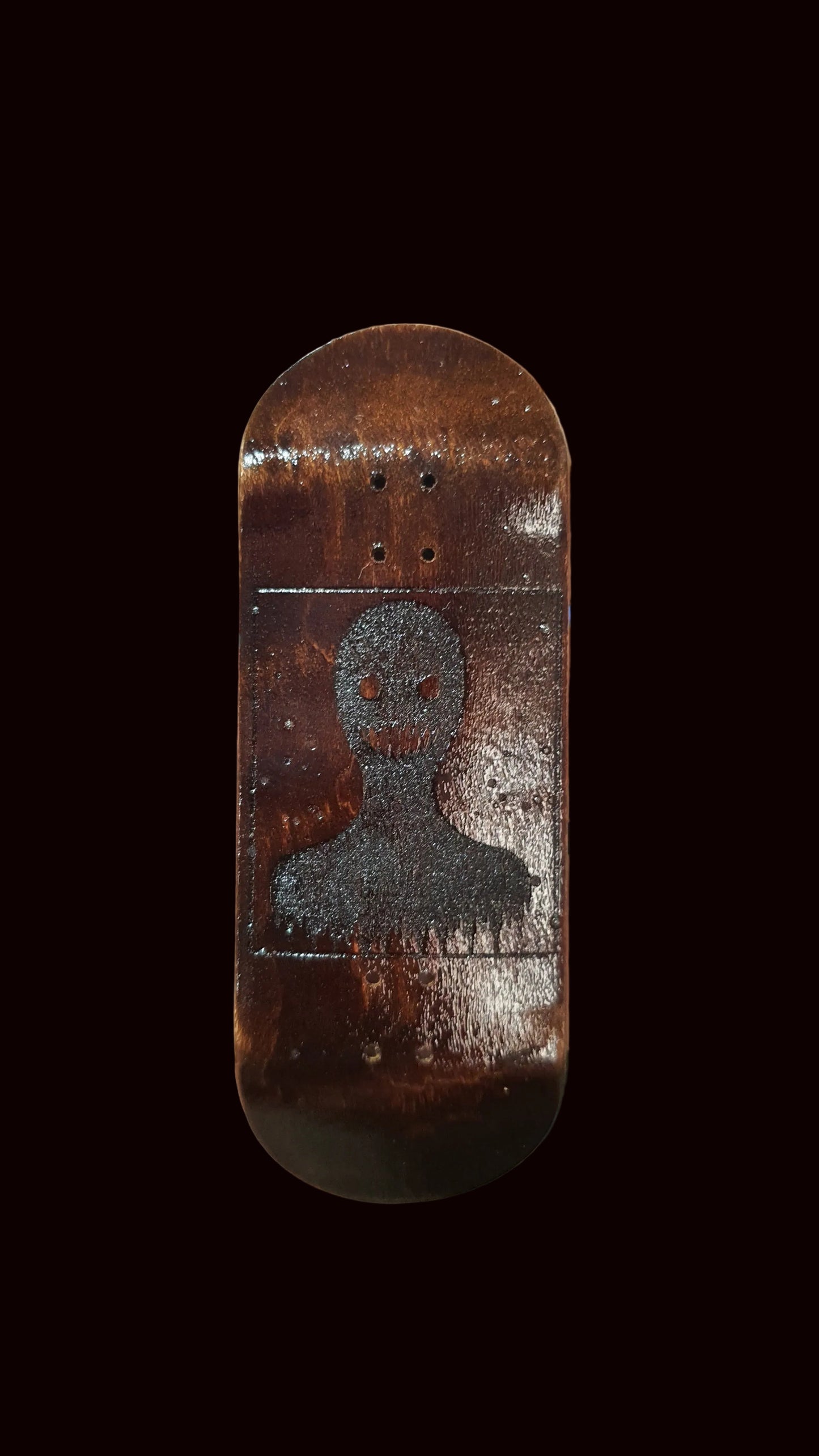 Hand holding a small wooden skateboard deck with a design on a blurred background
