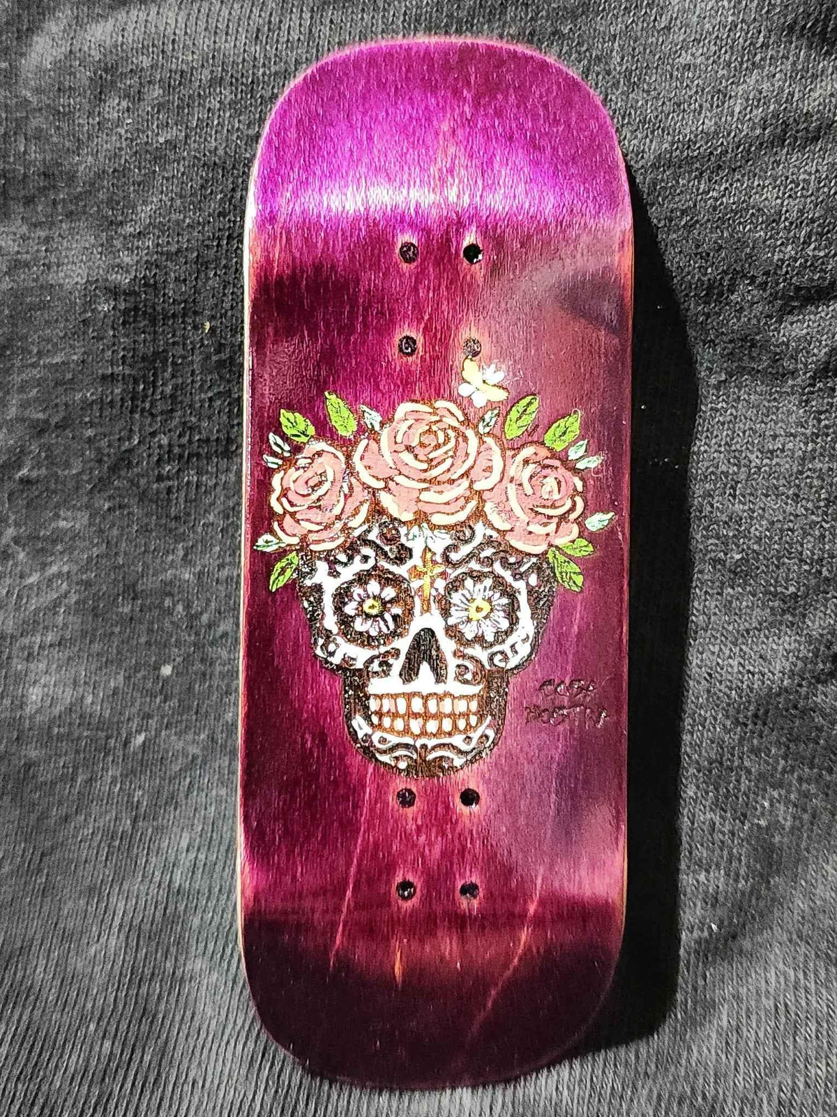 Handmade purple wooden fingerboard deck with a sugar skull and rose graphic.