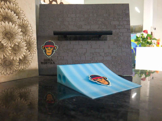 Blue fingerboard mini ramp ramp with a monkey sticker on a dark reflective surface.