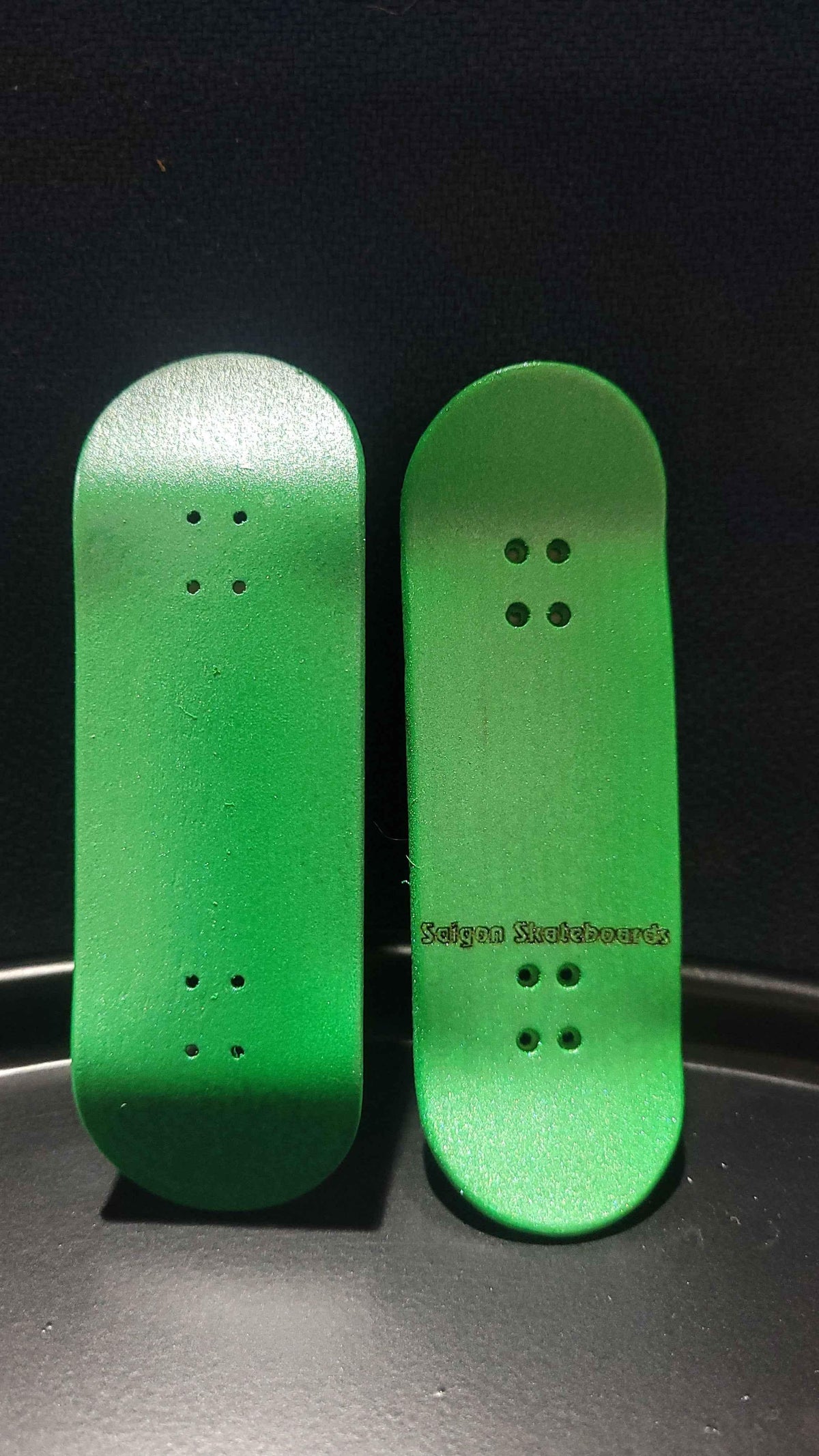 Two handmade green fingerboard decks with Saigon Skateboards branding on a dark background.