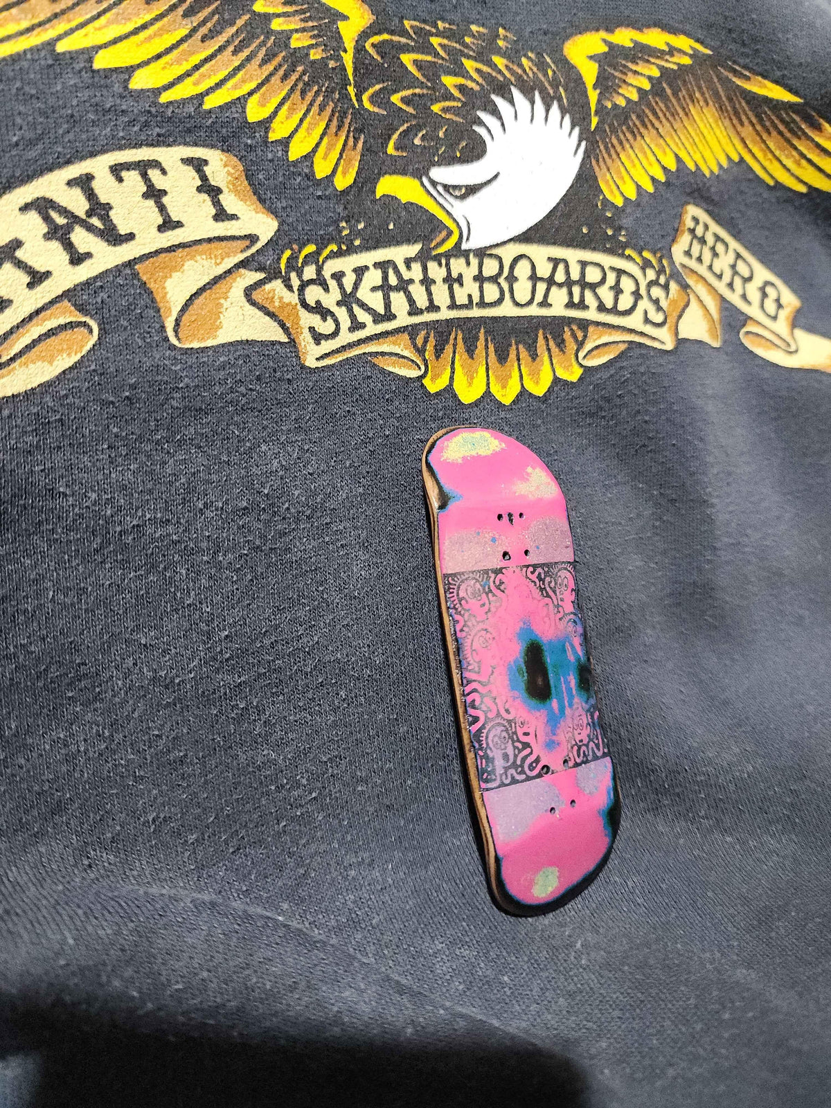 Custom pink graphic handmade fingerboard deck resting on a black graphic t-shirt.