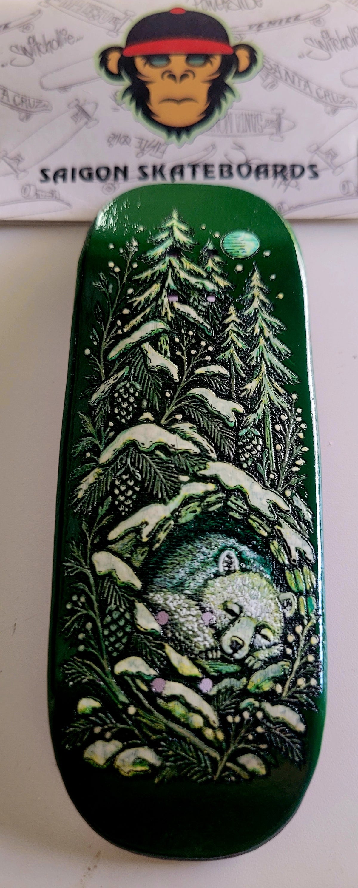 Dark green skateboard deck with night forest and moon graphic, rounded nose and tail