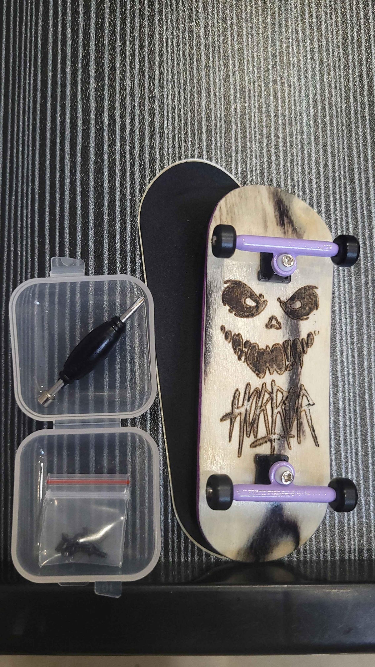 Custom handmade fingerboard with skull graphic, purple trucks, and assembly tool kit.