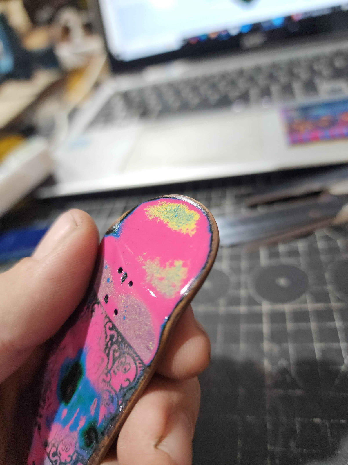 Hand holding a custom handmade pink fingerboard deck with colorful graphic art.