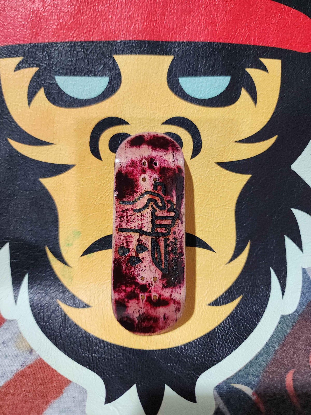 Handmade custom fingerboard deck with a maroon marble design and black graphic art.