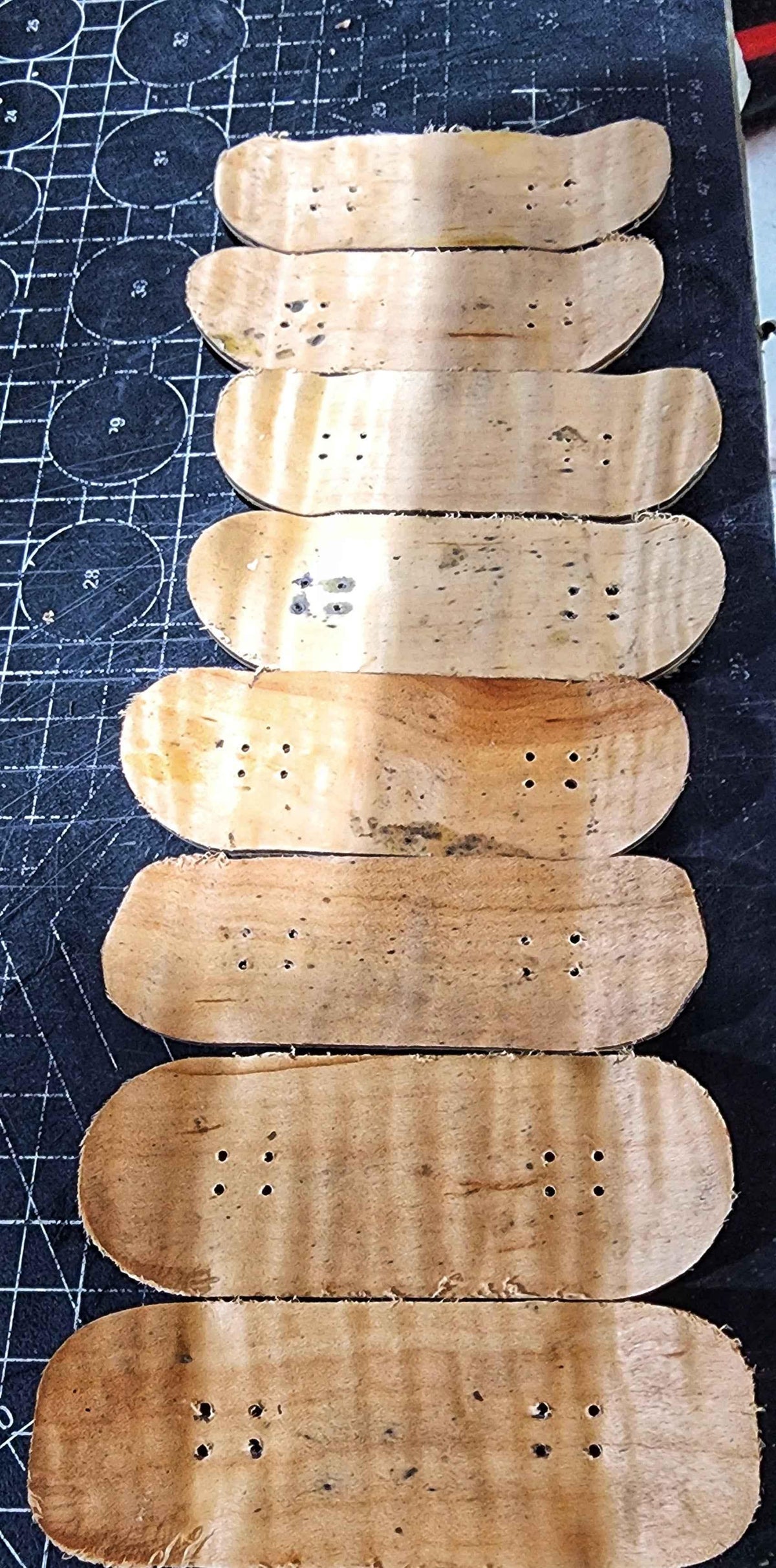 Collection of handmade wooden fingerboard decks on a cutting mat.
