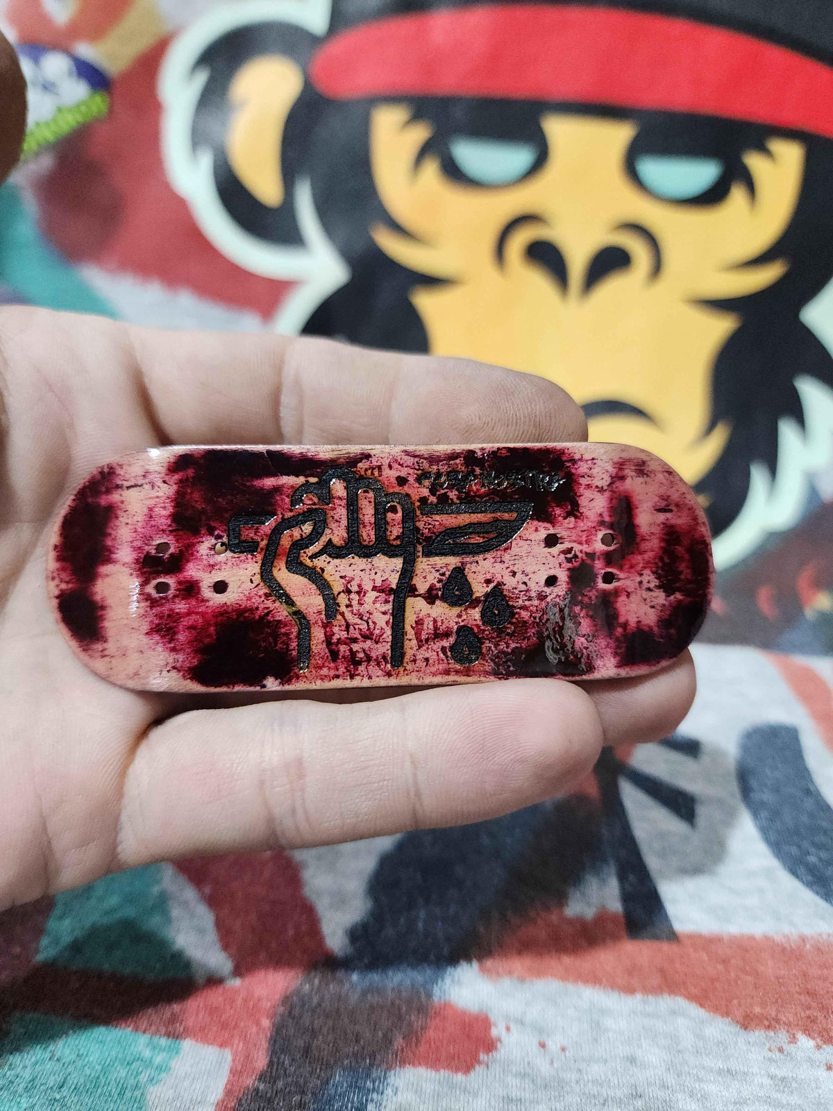 Hand holding a custom fingerboard deck with red splatter and a black graphic design