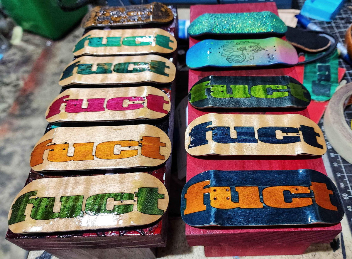 Custom handmade fingerboard decks with colorful graphic prints and various wood finishes.