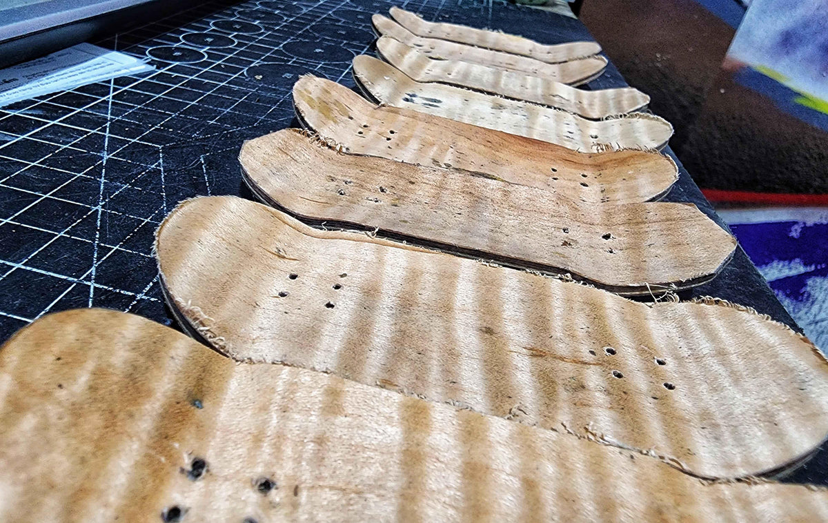 Row of handmade wooden fingerboard decks on a cutting mat during production.